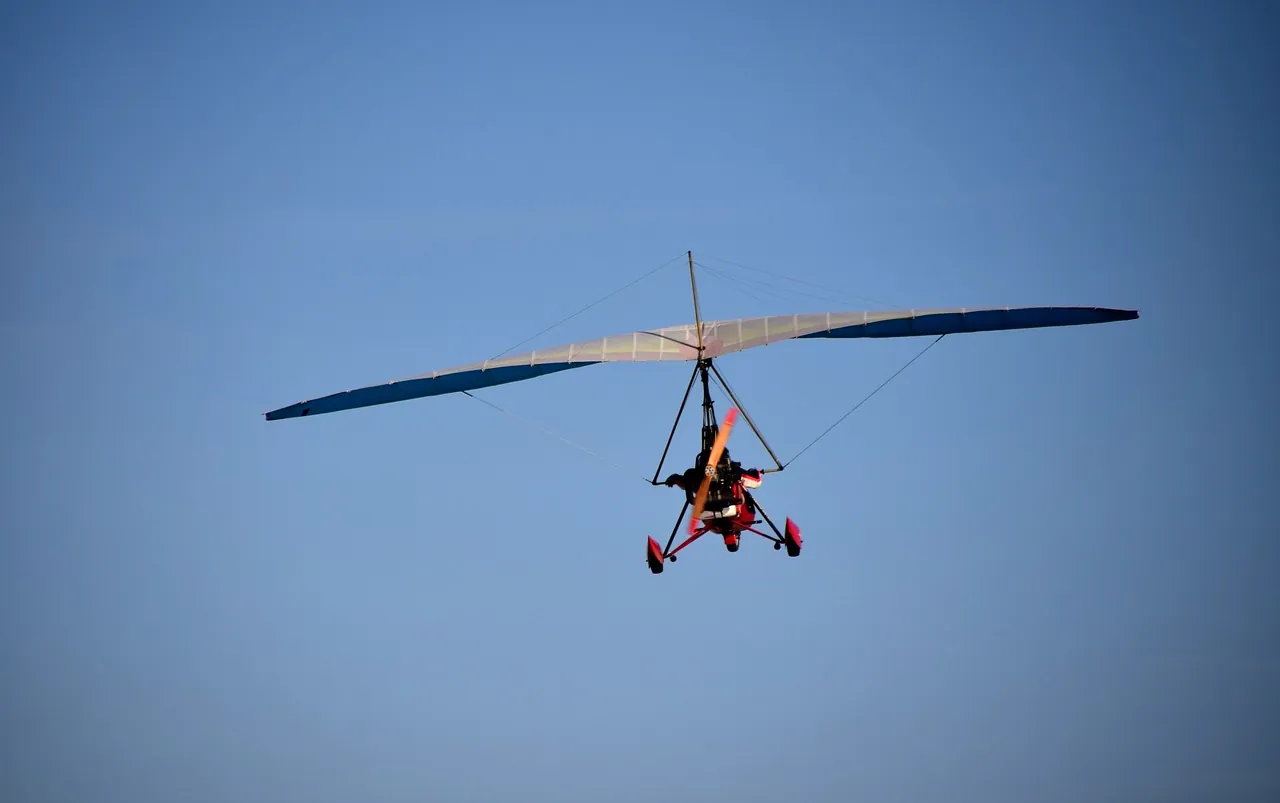 Un pilote deltaplane mi-vol, s'élançant sur un fond de nuages, utilisant trapèze pour décoller, courants d'air sous les ailes, lac serein au coucher du soleil comme site d'entraînement, ciel aventureux au-dessus